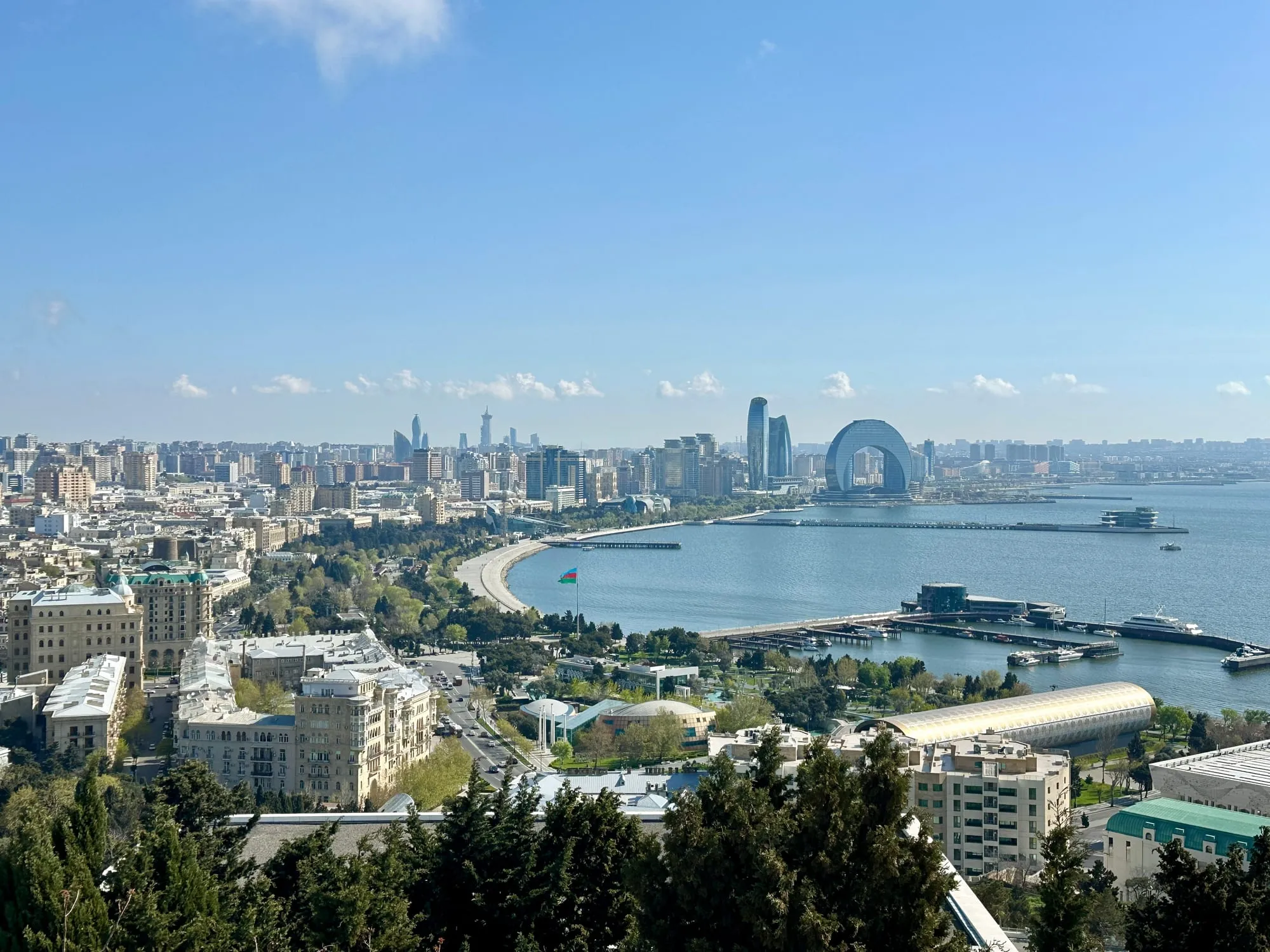 Panoramablick über Baku mit Hochhäusern, Uferpromenade, Hafenanlagen und der Bucht des Kaspischen Meeres.