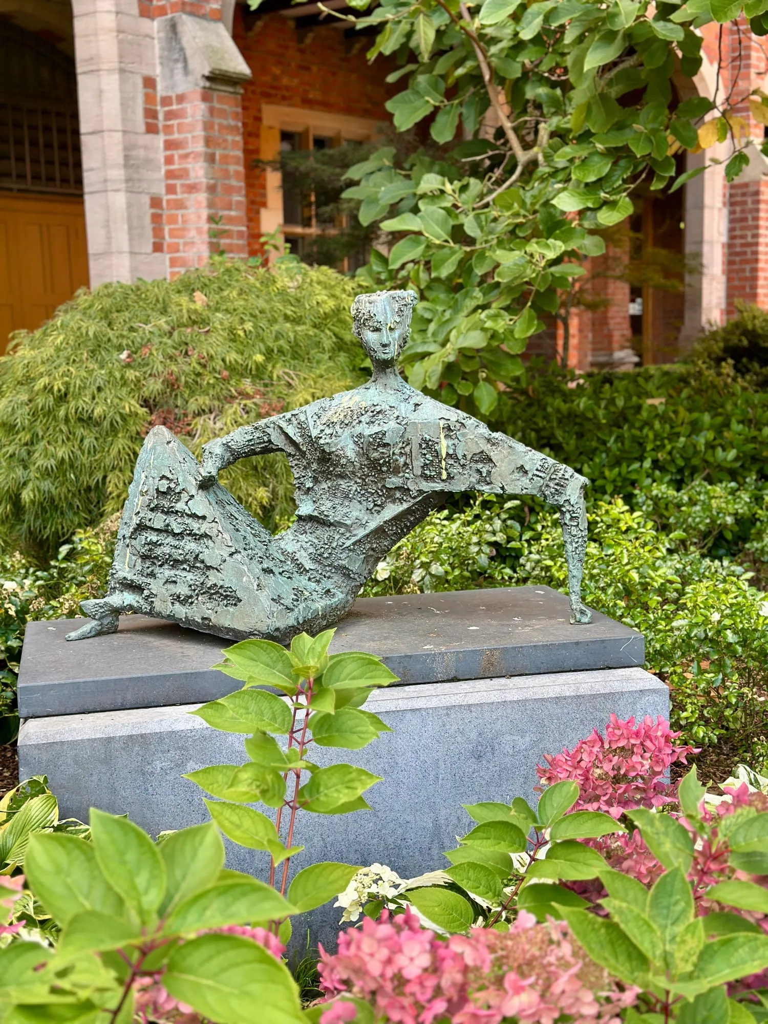 Bronzeskulptur einer liegenden Figur in einer Grünanlage der Queen's University Belfast.