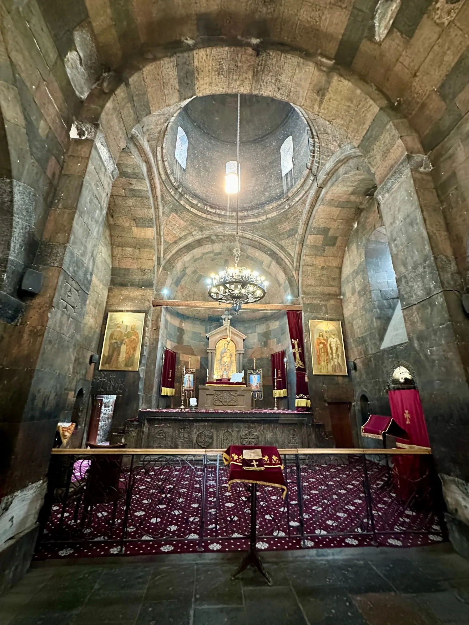 Steinerner Kircheninnenraum mit Kuppel, Kronleuchter, Ikonen und rotem Altarschmuck.