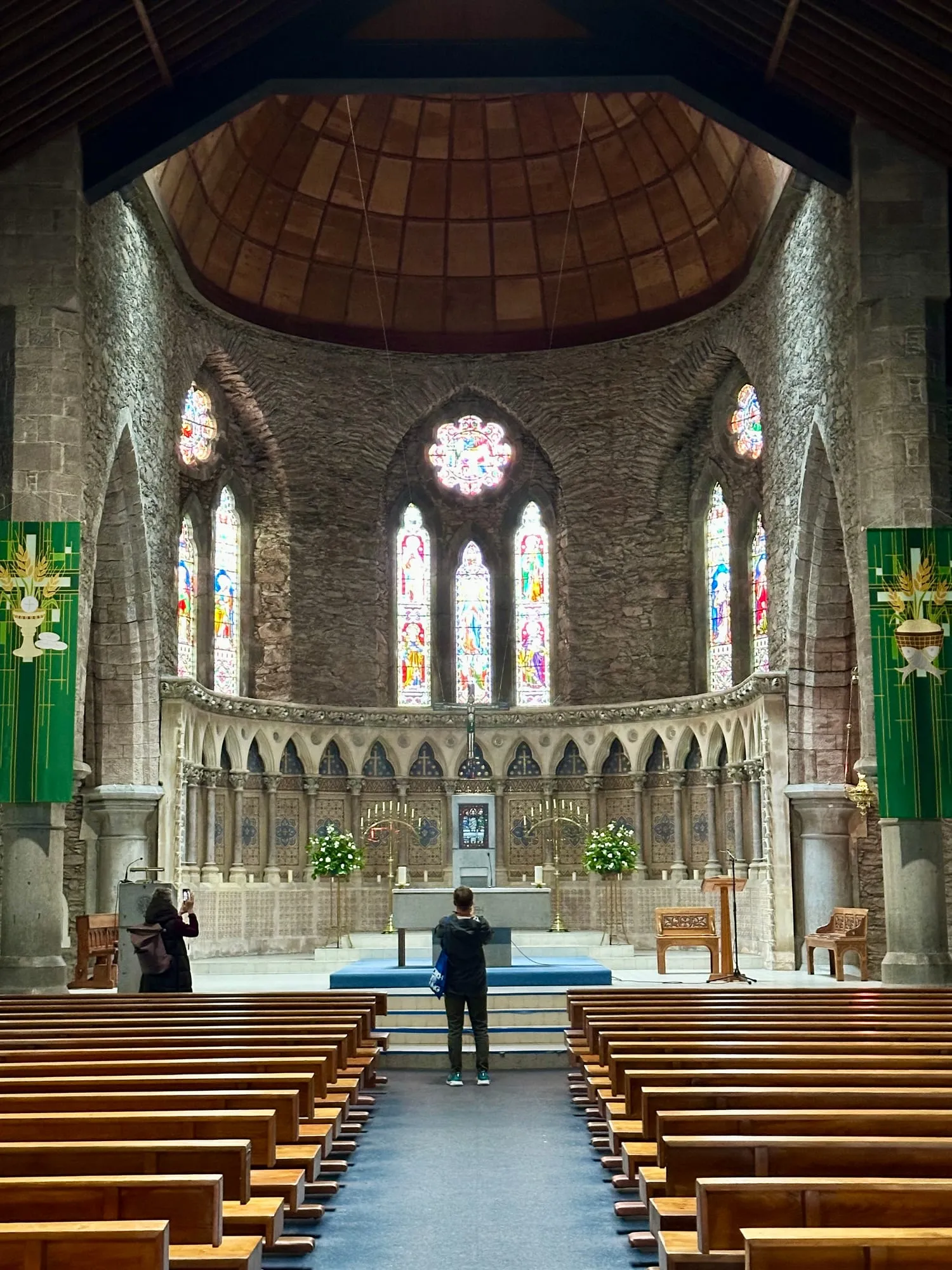 Innenraum einer Kirche in Dingle mit Buntglasfenstern und steinernem Chorbogen.