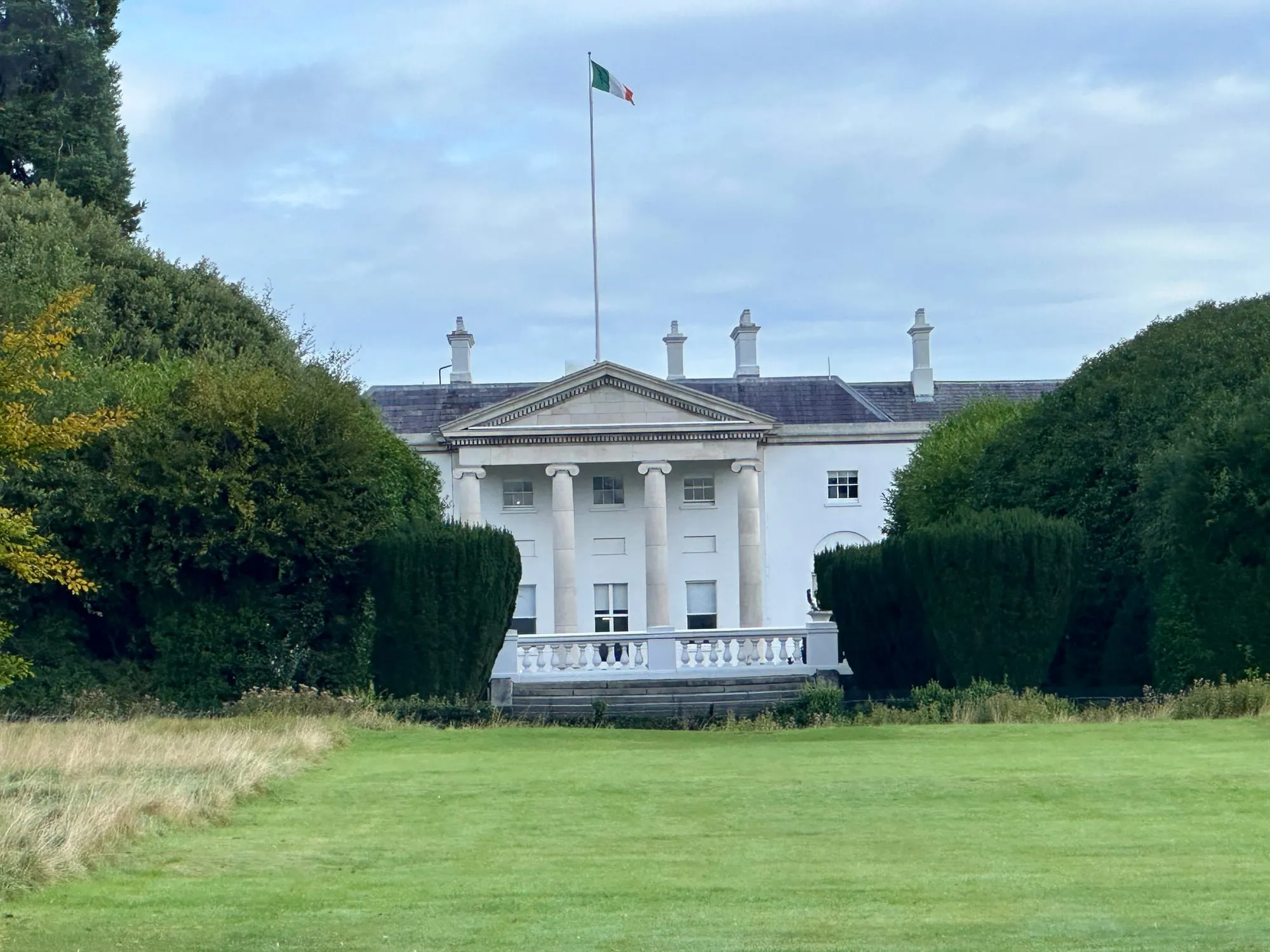 Weisses Herrenhaus mit Säulenvorbau und irischer Flagge im Phoenix Park in Dublin.