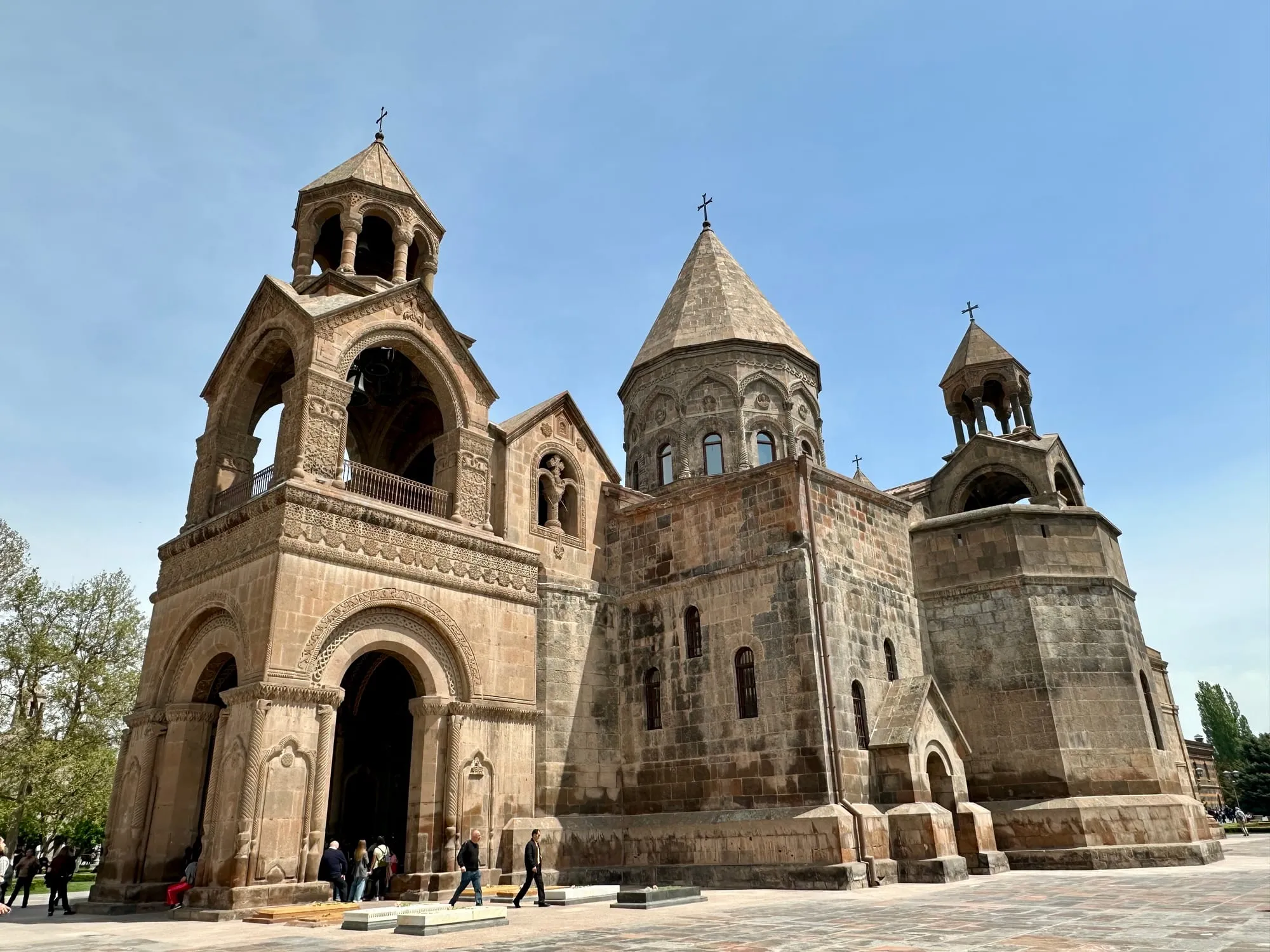 Reich verzierte armenische Kathedrale mit mehreren Türmen und Kreuzen, Besucher stehen davor auf einem gepflasterten Platz.