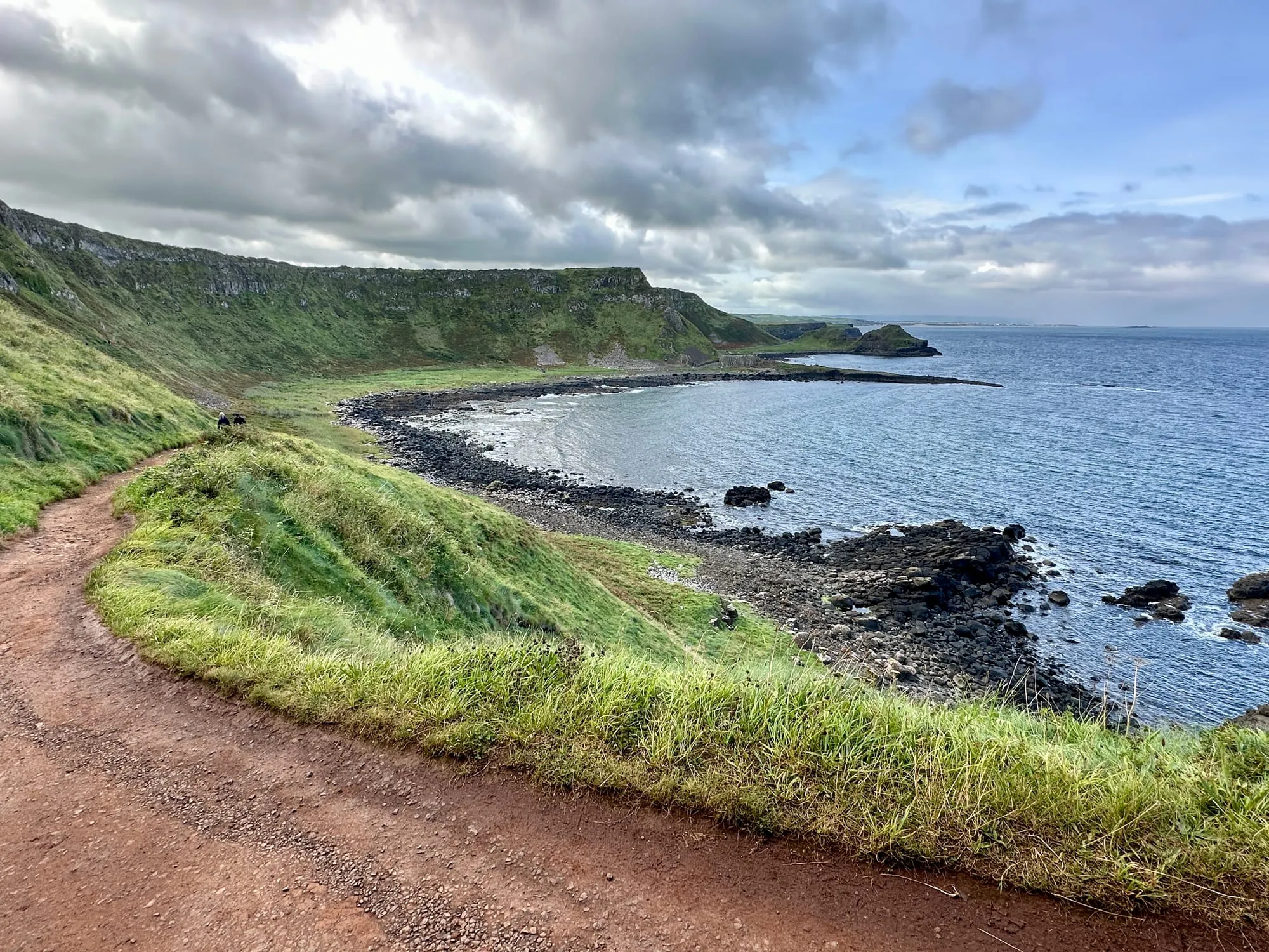 Küstenweg über einer Bucht, im Hintergrund die flache Landzunge des Giant's Causeway.