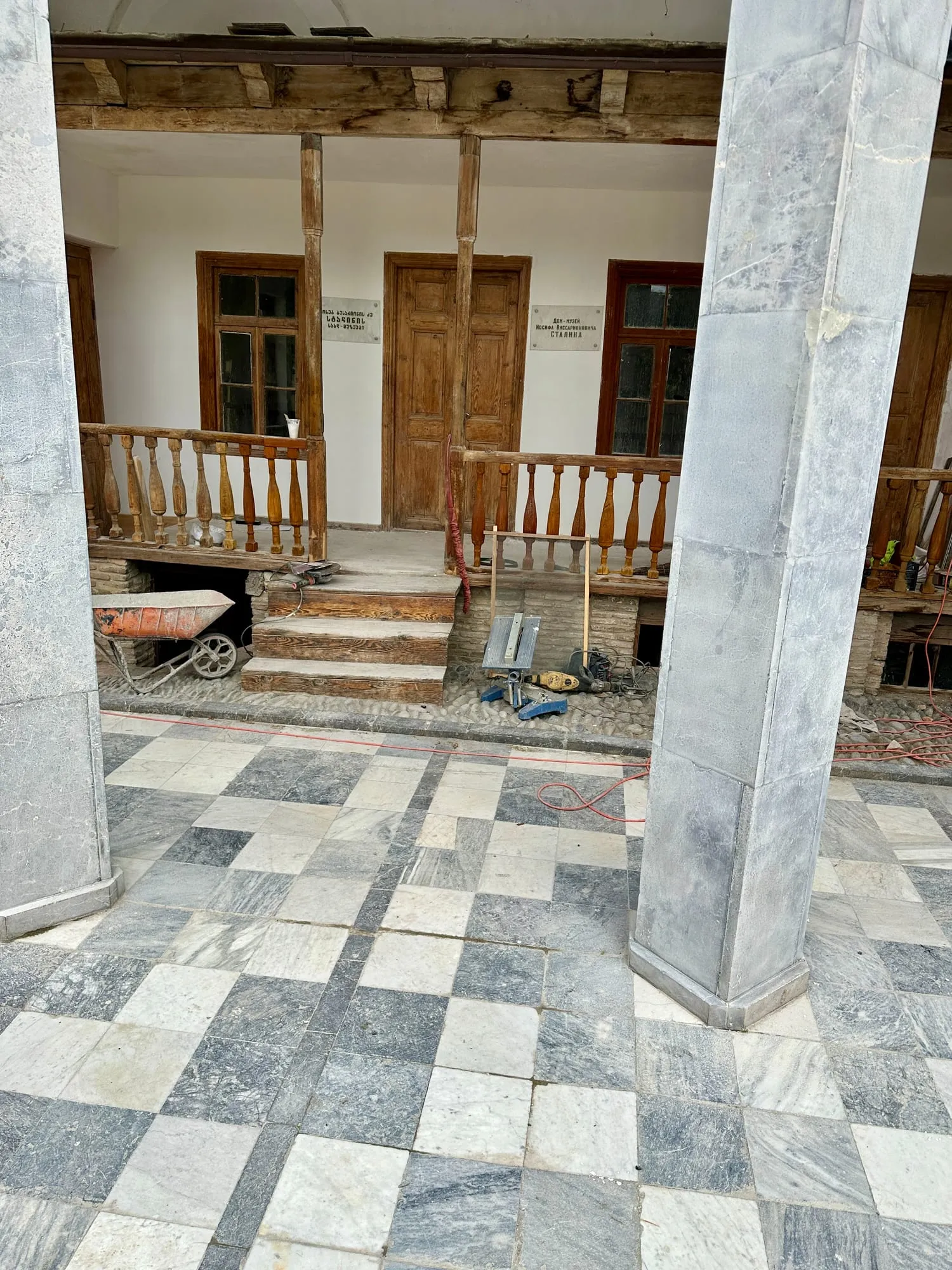 Hölzerne Veranda des als Stalin-Hausmuseum gekennzeichneten Geburtshauses mit zweisprachigen Schildern und steinernen Pfeilern.