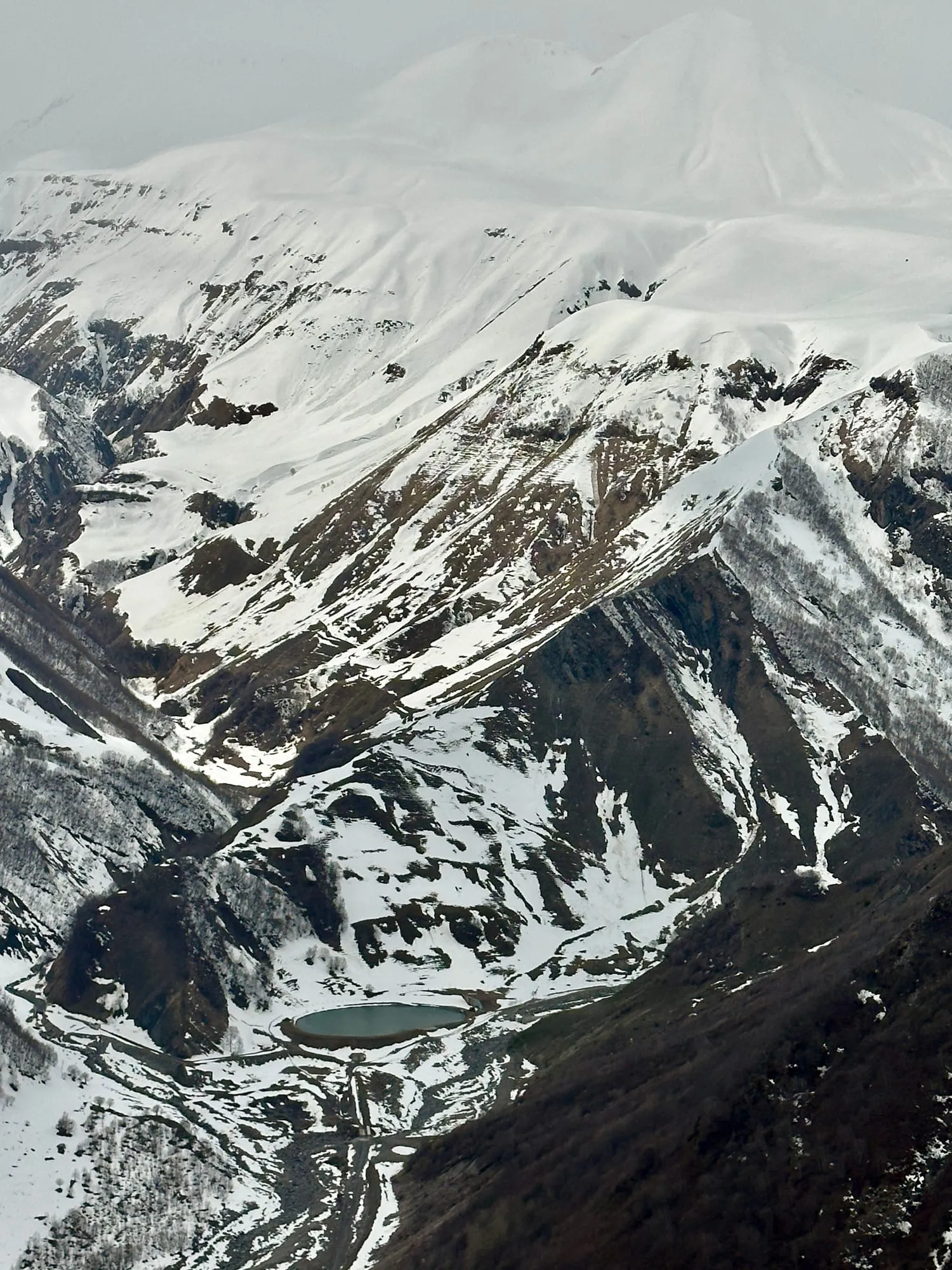 Steile verschneite Felsflanken mit einem kleinen ovalen Gewässer in einer Hochgebirgslandschaft.