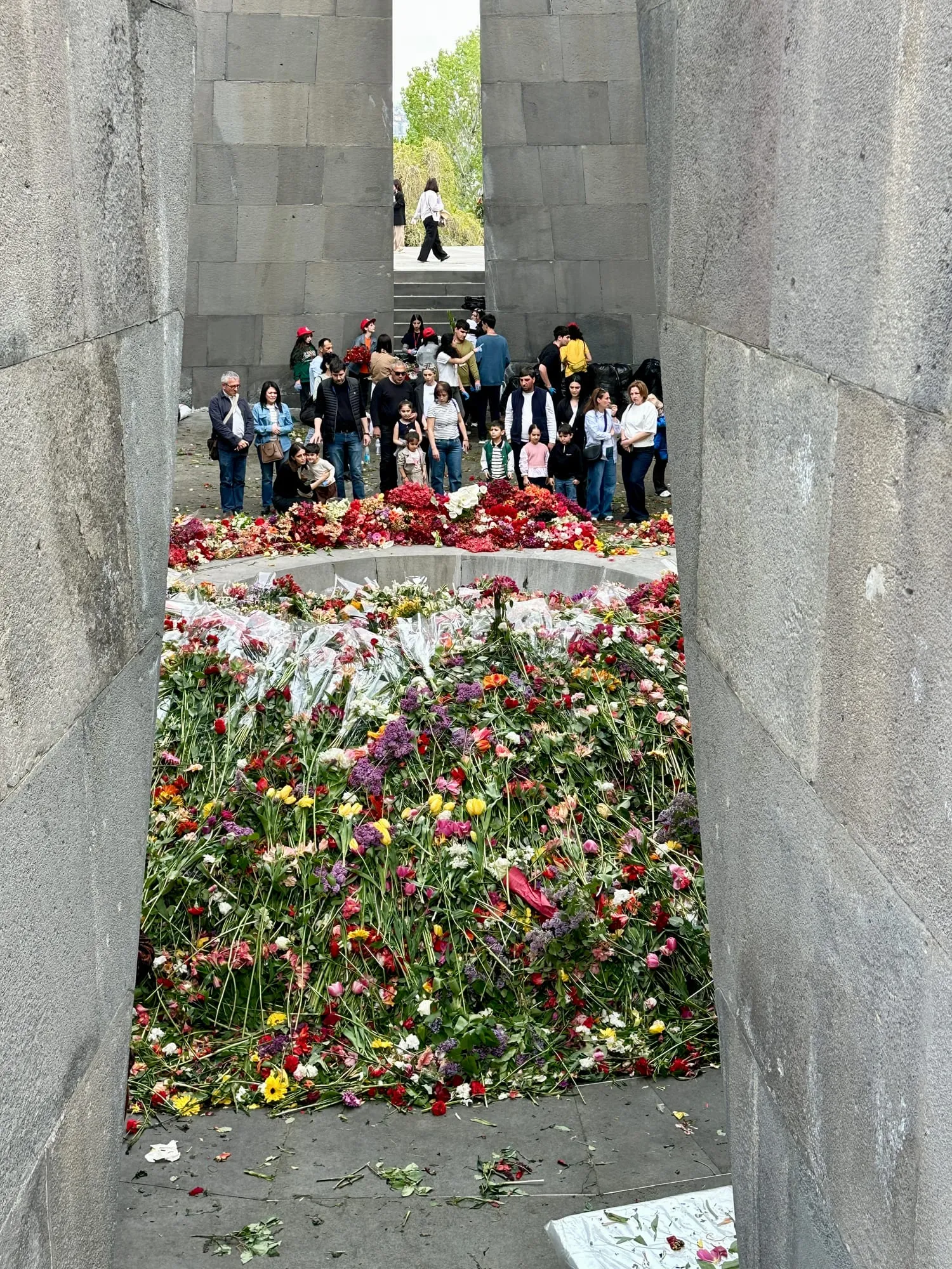 Zwischen hohen grauen Basaltplatten stehen zahlreiche Menschen hinter einem Meer aus bunten Blumen.