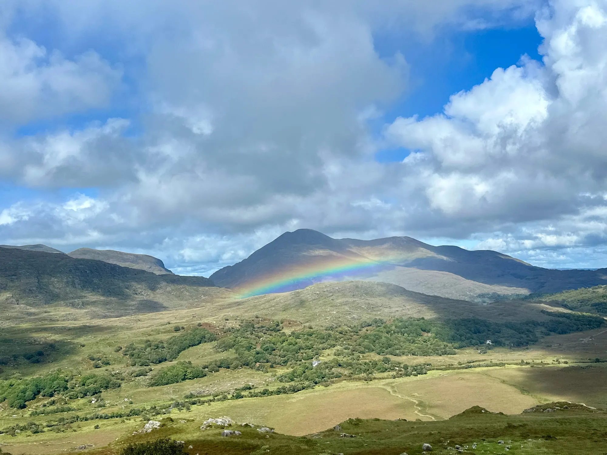 Regenbogen über den Bergen und Weiden von Kerry unter einer geschlossenen Wolkendecke.