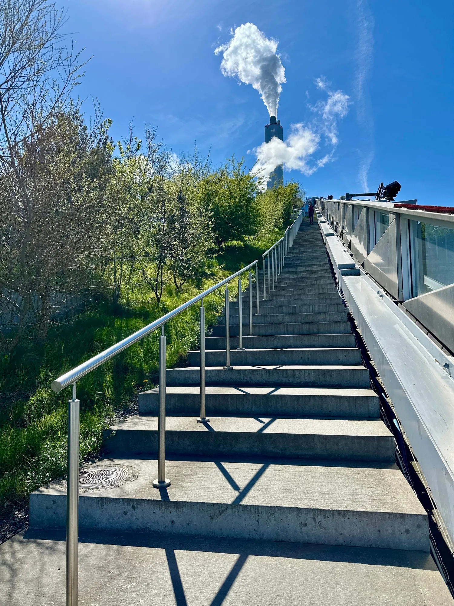Treppe entlang der begrünten Dachpiste von CopenHill mit dampfendem Schornstein.