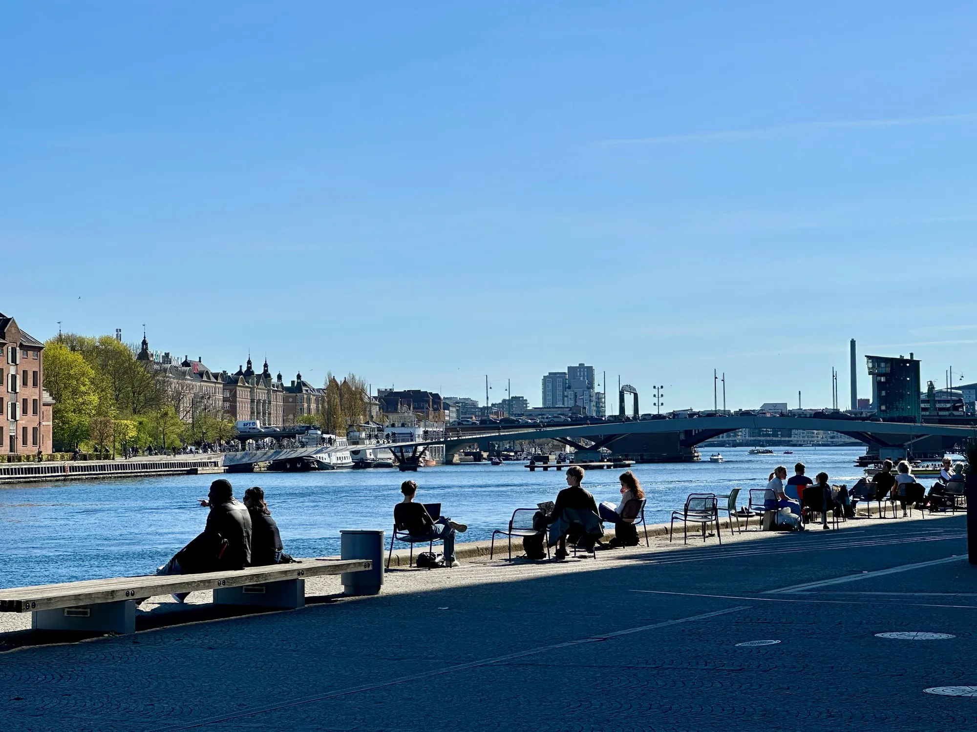 Menschen sitzen auf Stühlen an der Hafenpromenade in Kopenhagen in der Sonne.