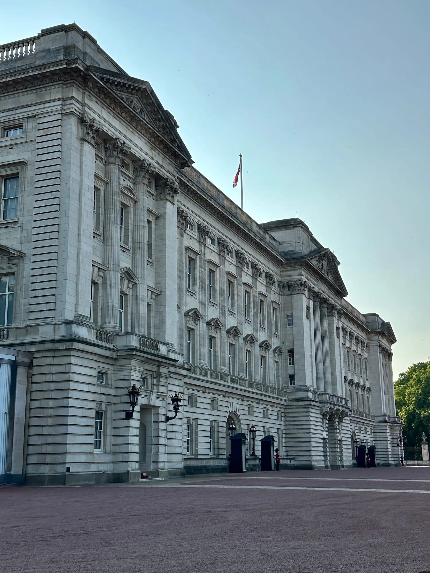Fassade des Buckingham Palace mit wehender Flagge und einem einzelnen Wachposten am Eingang.