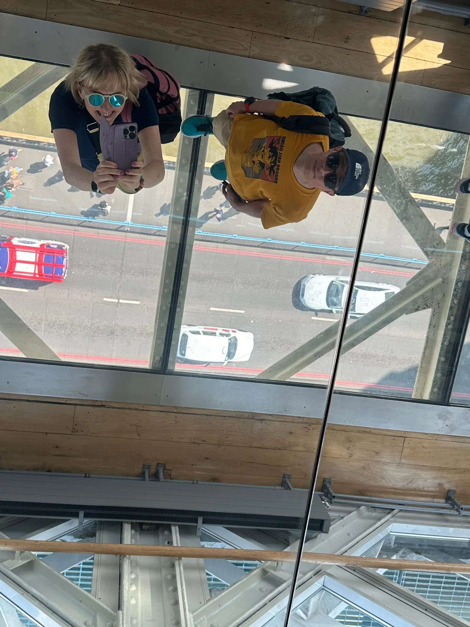 Zwei Personen stehen auf dem Glasboden der Tower Bridge, darunter Autos und ein Bus auf der Fahrbahn.