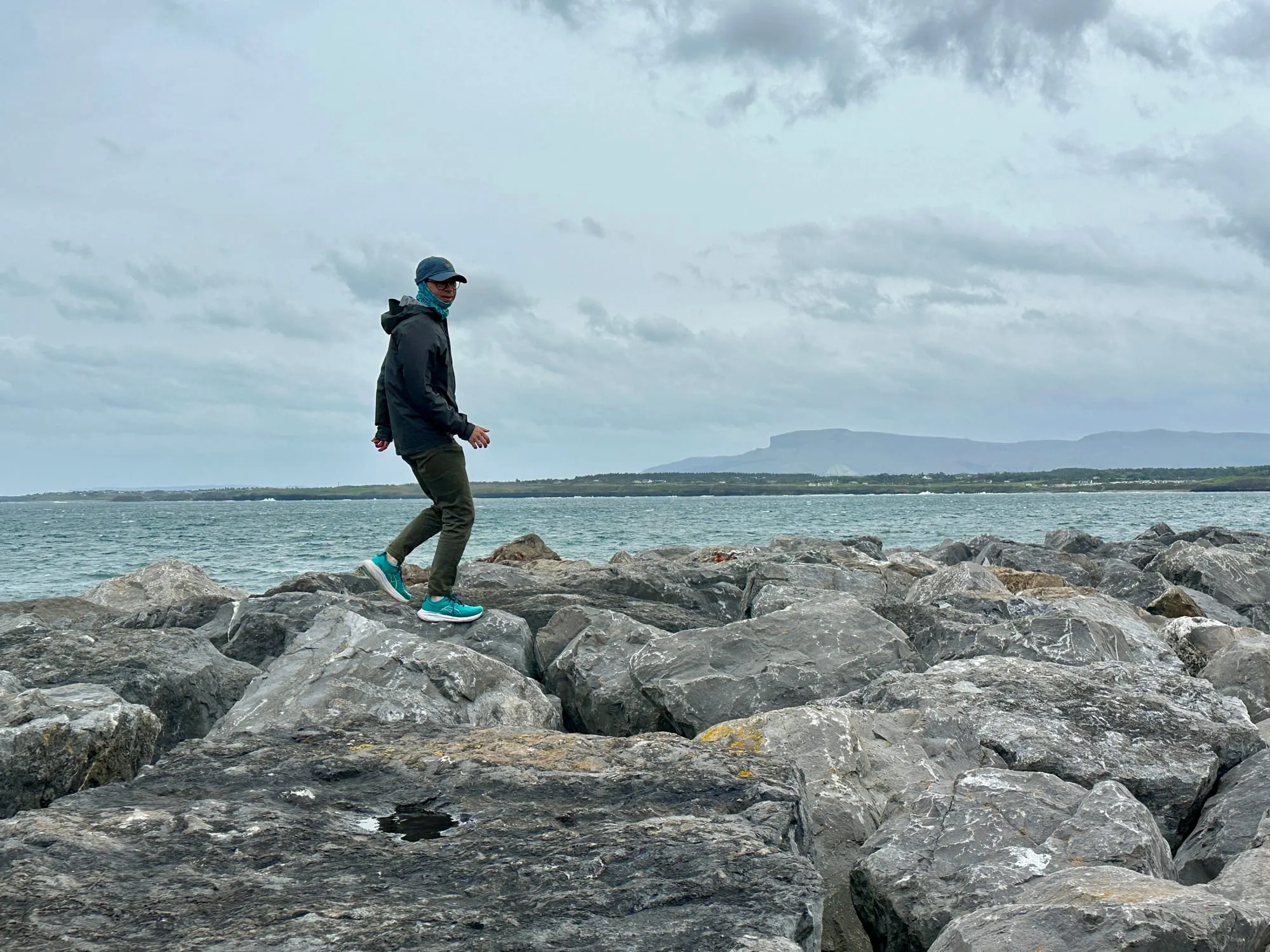 Person auf der Felsküste von Mullaghmore, im Hintergrund über der Bucht der Tafelberg Ben Bulben.