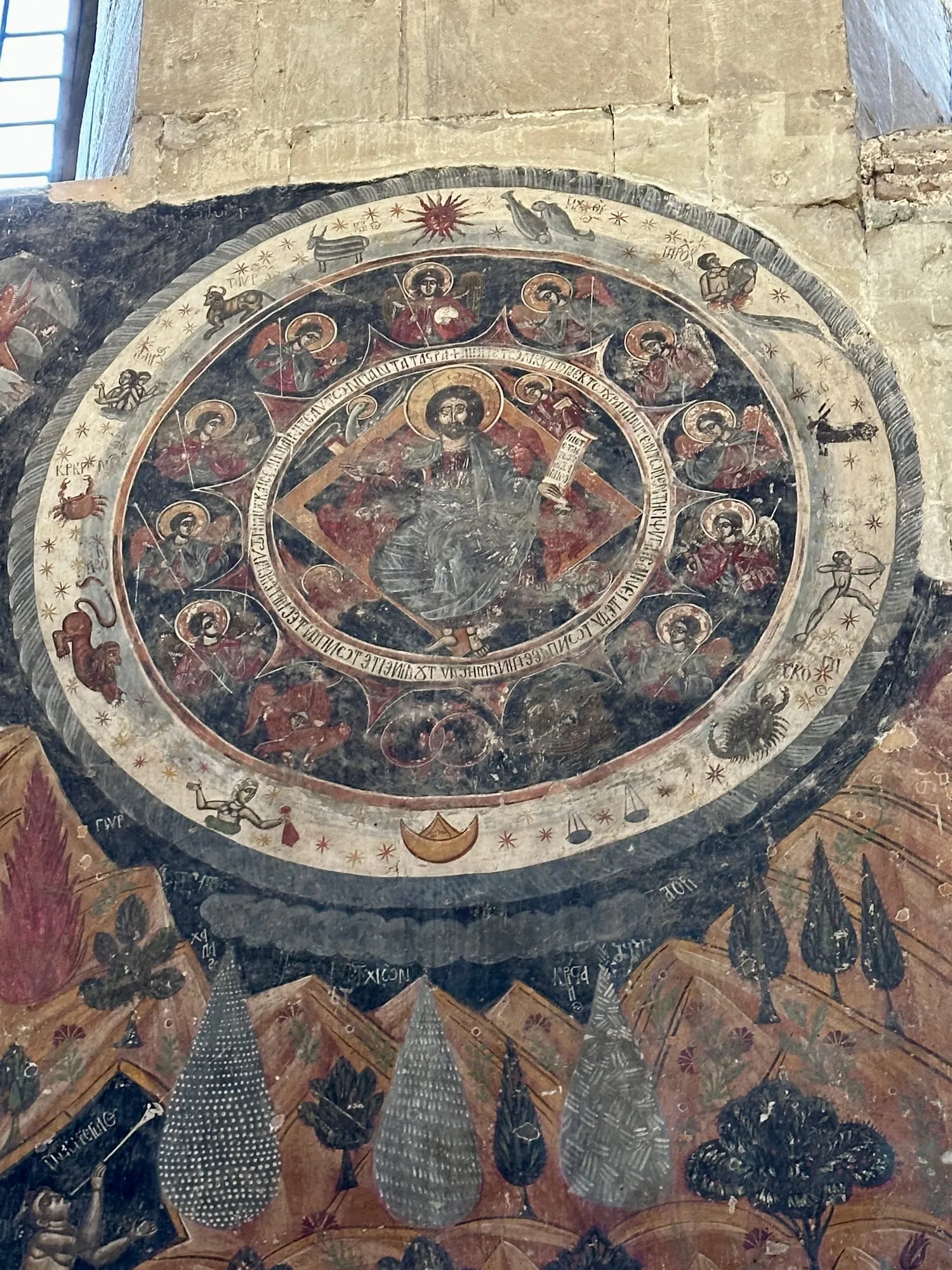 Nahaufnahme eines orthodoxen Kirchenfreskos mit konzentrischen Bildkreisen, Heiligenfiguren, Tieren, Sternen und Schriftbändern an einer Steinwand.