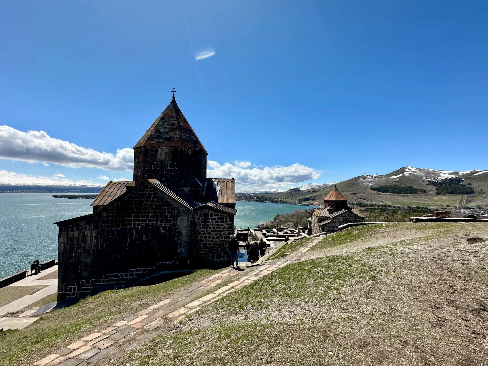 Dunkle Steinkirche des Klosters Sewanawank am Sewansee vor teils verschneiten Bergen.