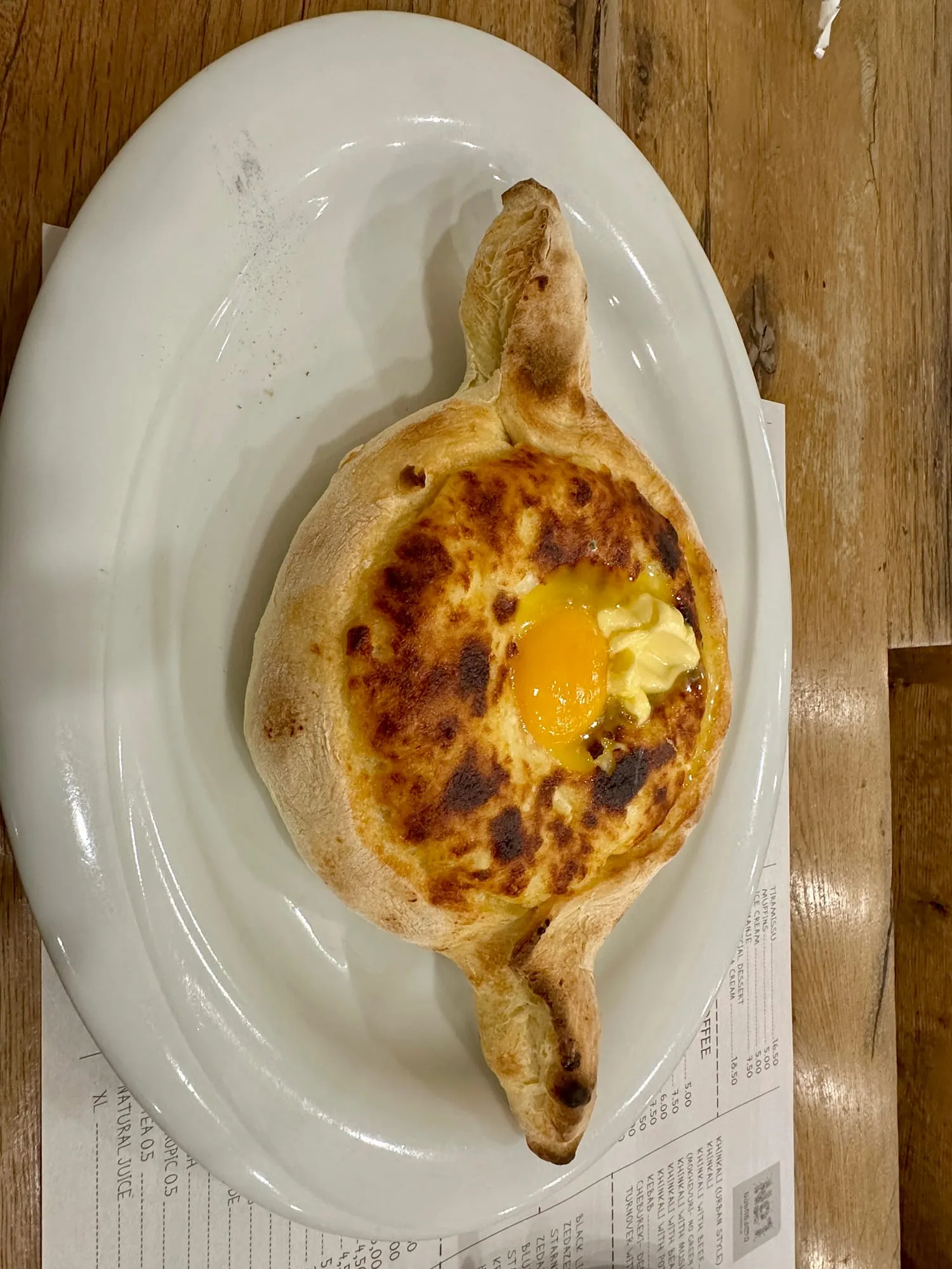 Bootförmiges Käsebrot mit flüssigem Eigelb und Butter auf einem weissen Teller.