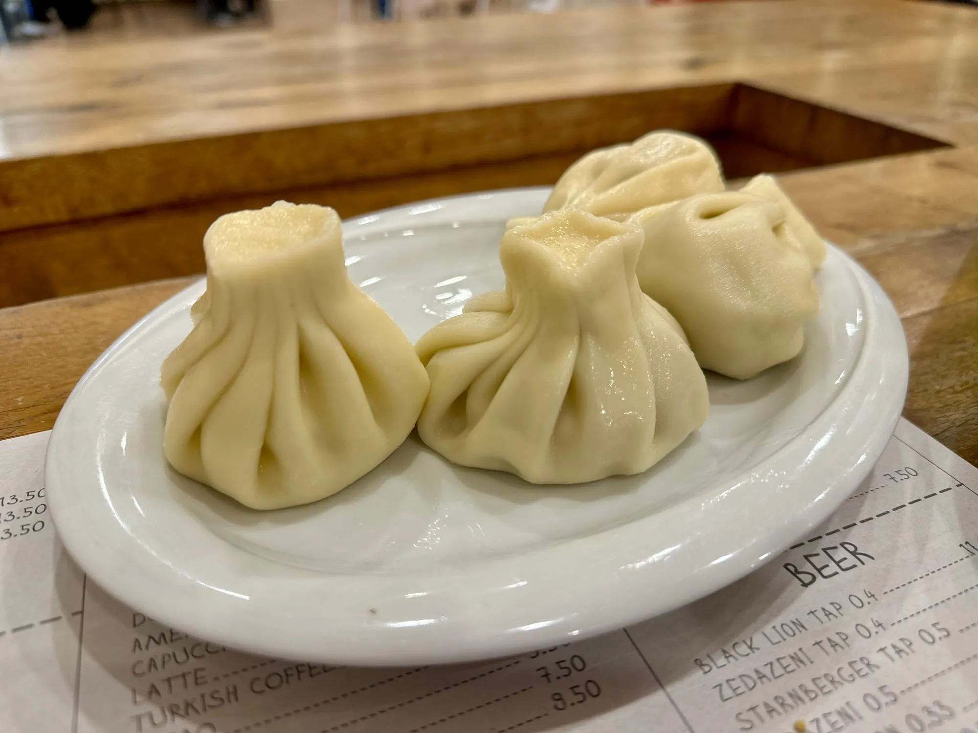 Mehrere gefaltete Chinkali liegen auf einem weissen Teller auf einem Holztisch.