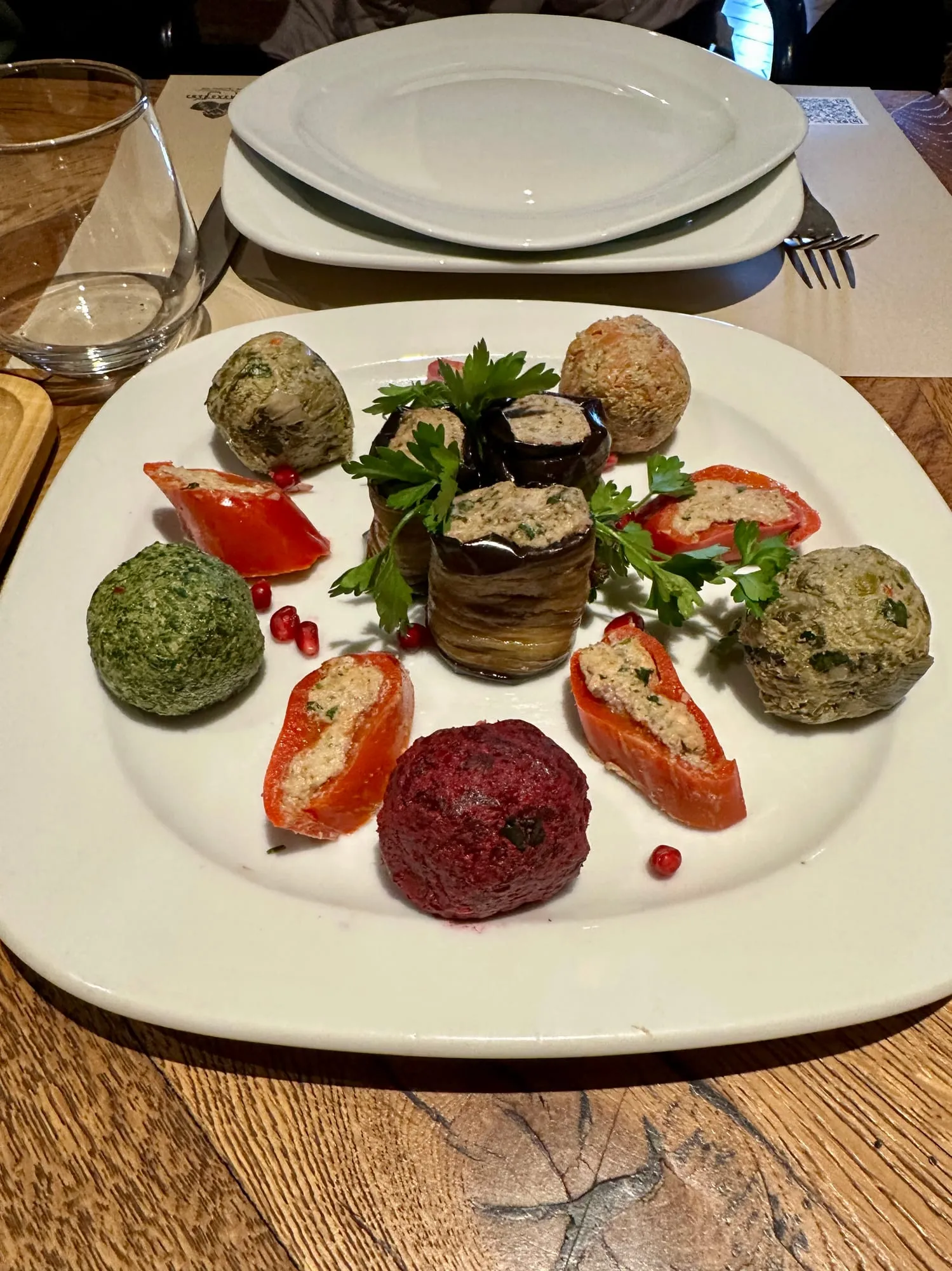Teller mit farbenfrohen georgischen Gemüsevorspeisen, gefüllten Auberginen und Tomaten sowie Granatapfelkernen.