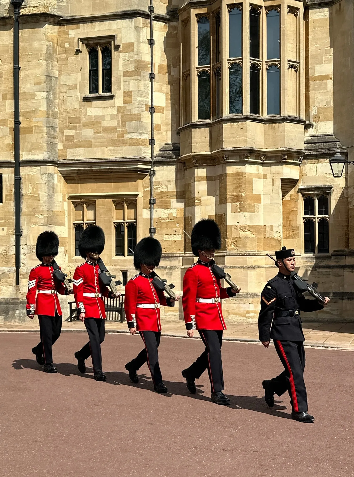 Fünf Gardisten in roten Uniformen mit Bärenfellmützen marschieren durch Windsor Castle.