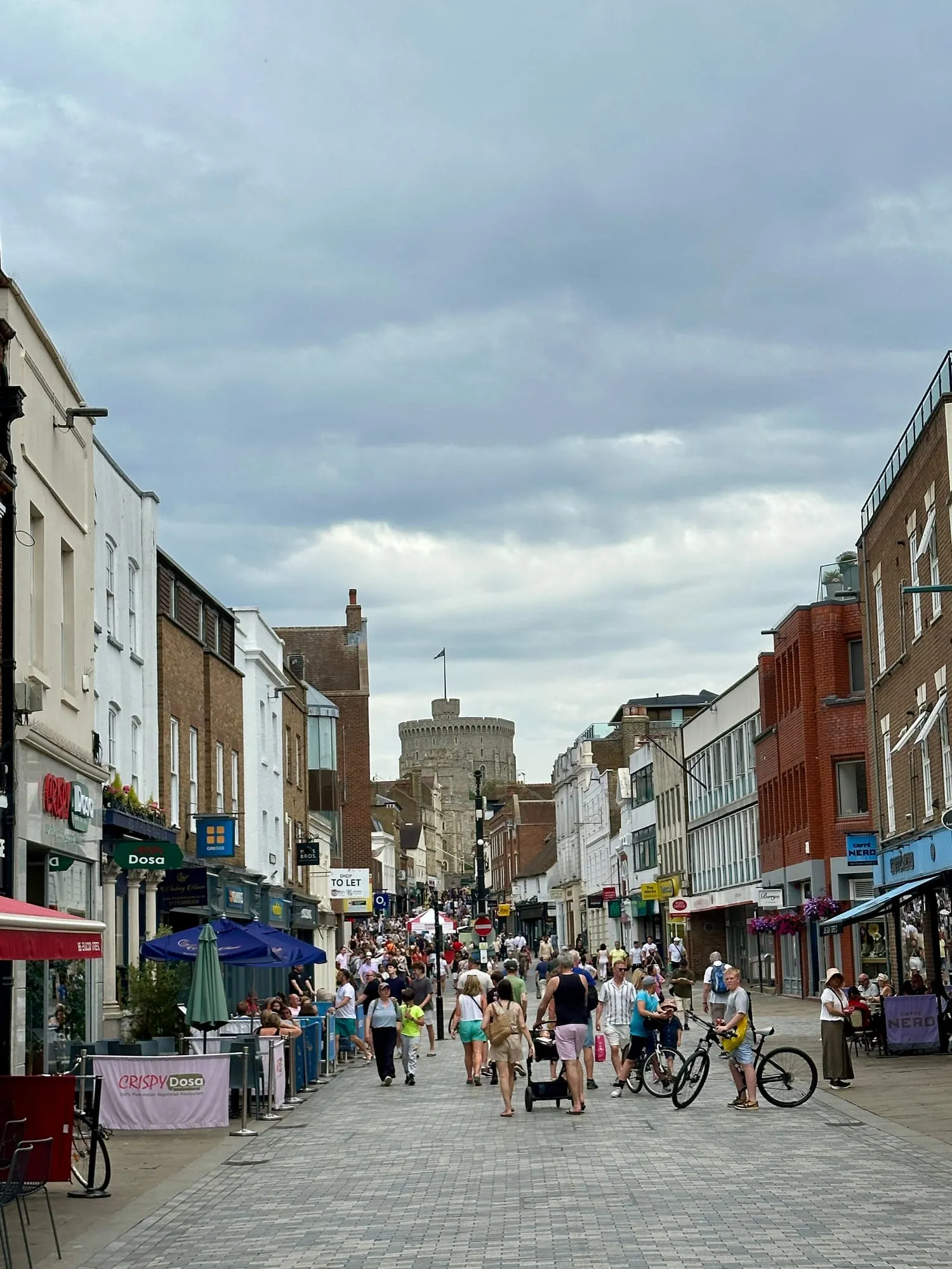 Belebte Fussgängerzone in Windsor mit dem Round Tower der Burg im Hintergrund.